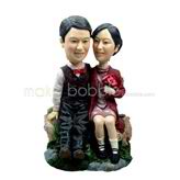 The couple sit on a stone custom bobbleheads