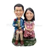 The couple sit on a stone custom bobbleheads